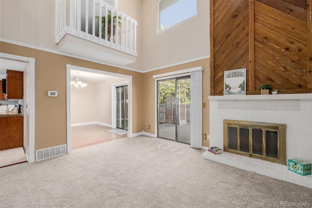 unfurnished living room featuring a towering ceiling, an inviting chandelier, carpet floors, and a brick fireplace