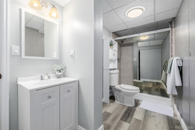 bathroom with a paneled ceiling, wood-type flooring, toilet, vanity, and an enclosed shower