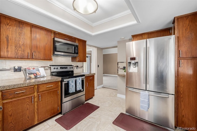 kitchen with crown molding, stainless steel appliances, a tray ceiling, and backsplash