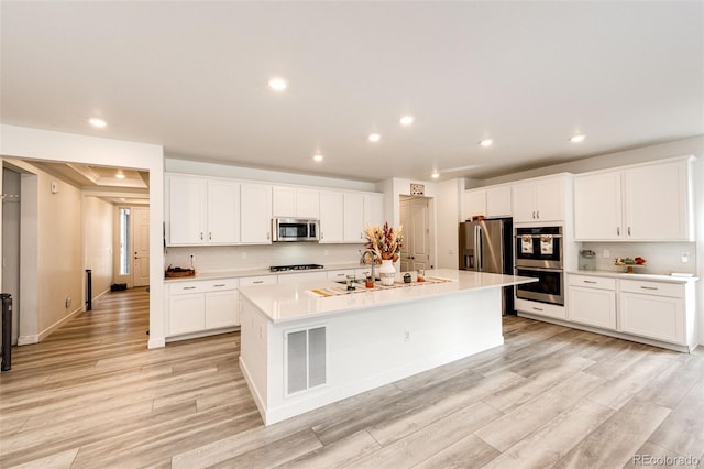 kitchen featuring white cabinets, an island with sink, light hardwood / wood-style floors, and appliances with stainless steel finishes