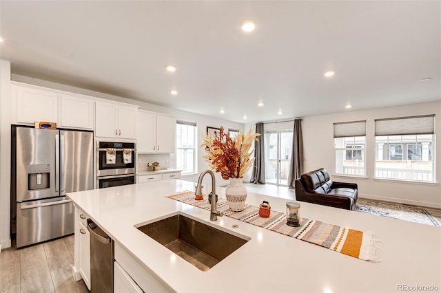 kitchen with white cabinetry, sink, stainless steel appliances, and light hardwood / wood-style flooring