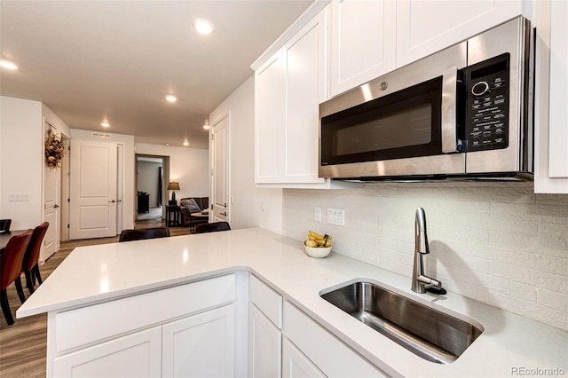 kitchen with white cabinets, backsplash, kitchen peninsula, and sink