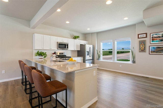 7407 Rufous Fronted Vw, Colorado Springs, CO 80923 - kitchen with appliances with stainless steel finishes, a breakfast bar, wood finished floors, white cabinets, and backsplash