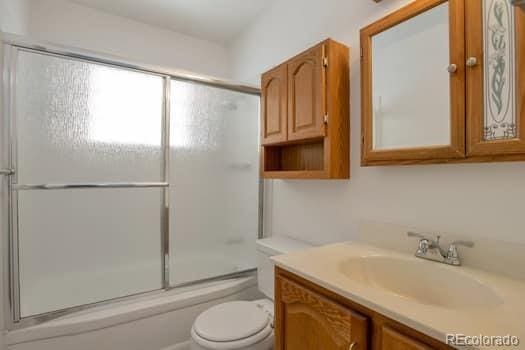 full bathroom with enclosed tub / shower combo, vanity, and toilet