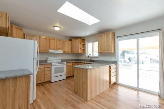 kitchen with light brown cabinetry, sink, a skylight, light hardwood / wood-style flooring, and white appliances