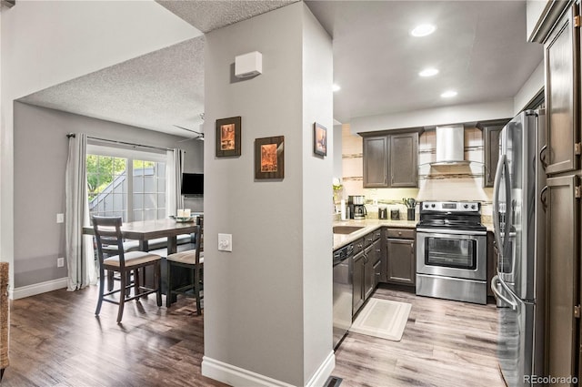 943 S Fairplay St, Aurora, CO 80012 - kitchen with stainless steel appliances, wall chimney exhaust hood, wood finished floors, baseboards, and recessed lighting