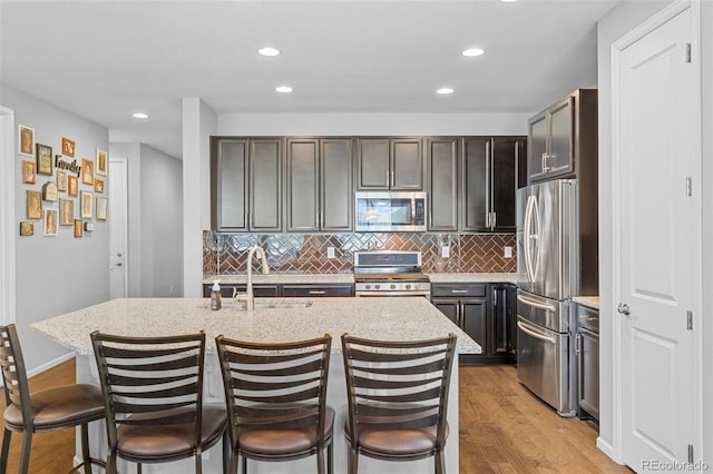 15895 Columbine St, Thornton, CO 80602 - kitchen featuring appliances with stainless steel finishes, light wood-type flooring, a kitchen bar, backsplash, and light stone counters