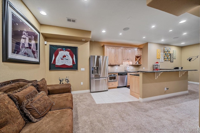 8655 E 130th Ave, Thornton, CO 80602 - kitchen with stainless steel appliances, light brown cabinetry, light colored carpet, a kitchen bar, and dark countertops