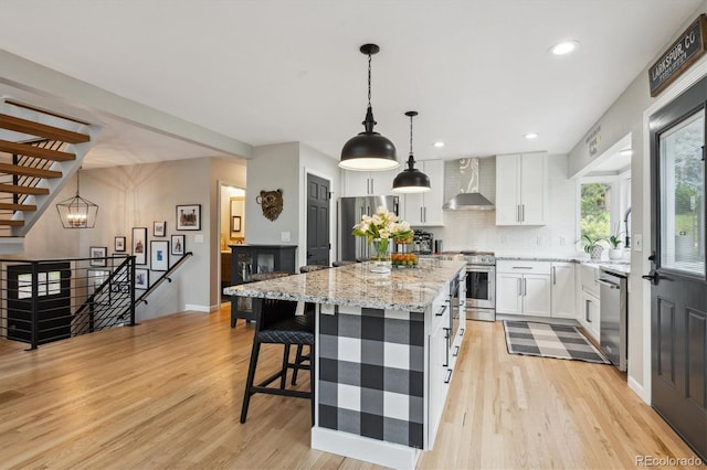 7312 Marshall Rd, Larkspur, CO 80118 - kitchen featuring stainless steel appliances, wall chimney exhaust hood, light wood-type flooring, decorative backsplash, and white cabinetry