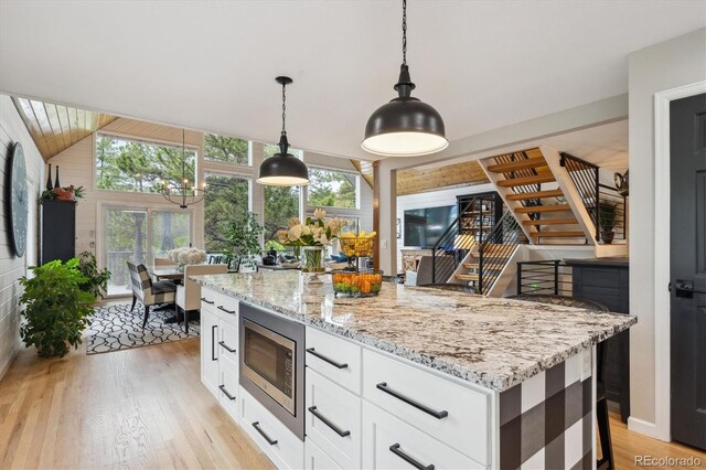 7312 Marshall Rd, Larkspur, CO 80118 - kitchen featuring stainless steel microwave, light wood finished floors, healthy amount of natural light, light stone countertops, and lofted ceiling