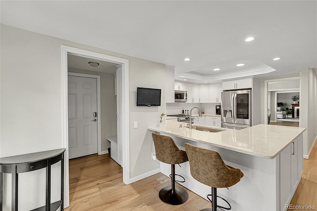 kitchen with appliances with stainless steel finishes, a sink, light wood finished floors, a tray ceiling, and white cabinets