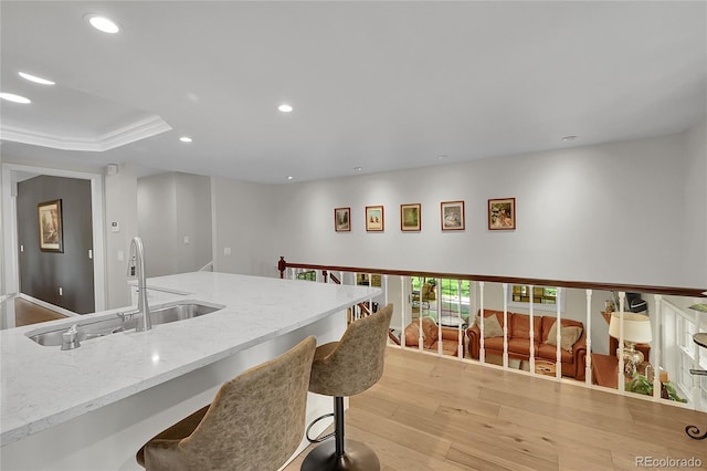 kitchen with a sink, light wood finished floors, recessed lighting, light stone countertops, and a kitchen breakfast bar