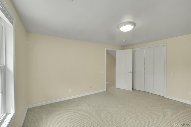 unfurnished bedroom featuring baseboards, light carpet, and a closet