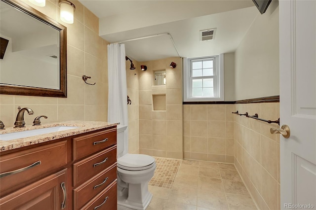 bathroom with tile walls, toilet, tiled shower, and vanity