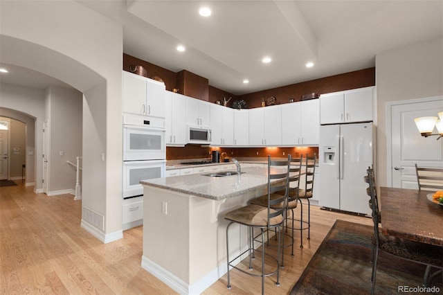 652 Ulster Way, Denver, CO 80230 - kitchen with white appliances, a sink, arched walkways, light wood finished floors, and a center island with sink