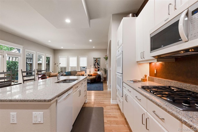 652 Ulster Way, Denver, CO 80230 - kitchen featuring white appliances, a sink, light wood-type flooring, open floor plan, and an island with sink