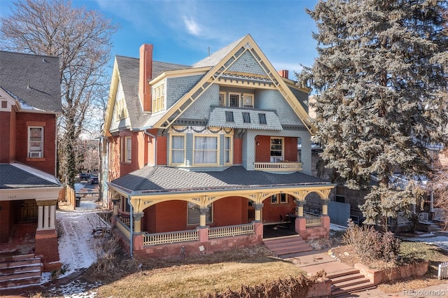 victorian home with covered porch, brick siding, and a shingled roof