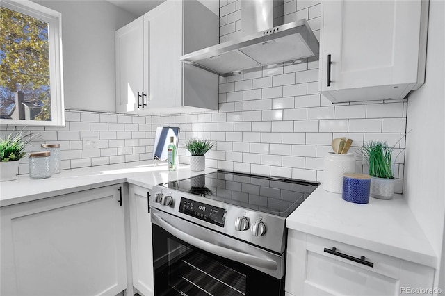 kitchen featuring white cabinetry, wall chimney range hood, stainless steel range with electric cooktop, and tasteful backsplash