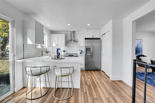 kitchen with white cabinetry, sink, stainless steel appliances, wall chimney range hood, and light wood-type flooring