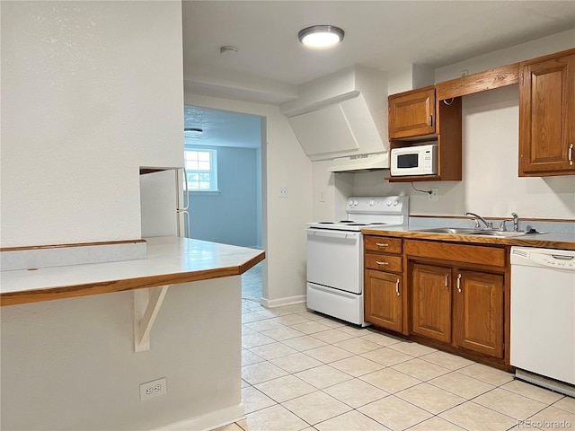 kitchen with custom exhaust hood, white appliances, sink, light tile patterned floors, and kitchen peninsula