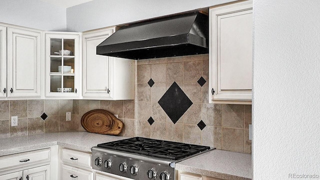 kitchen featuring backsplash, wall chimney exhaust hood, light countertops, glass insert cabinets, and stove