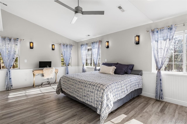 bedroom with visible vents, wainscoting, wood finished floors, and vaulted ceiling