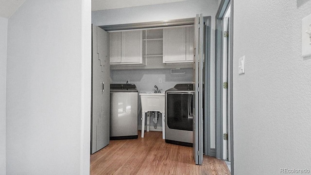 clothes washing area featuring light wood finished floors, cabinet space, a textured wall, and washing machine and clothes dryer