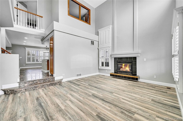 unfurnished living room featuring a tiled fireplace, wood finished floors, visible vents, and baseboards