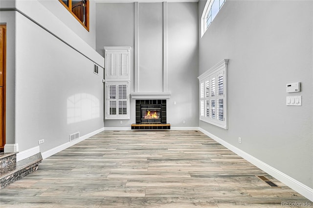 unfurnished living room featuring visible vents, a tiled fireplace, wood finished floors, baseboards, and a towering ceiling