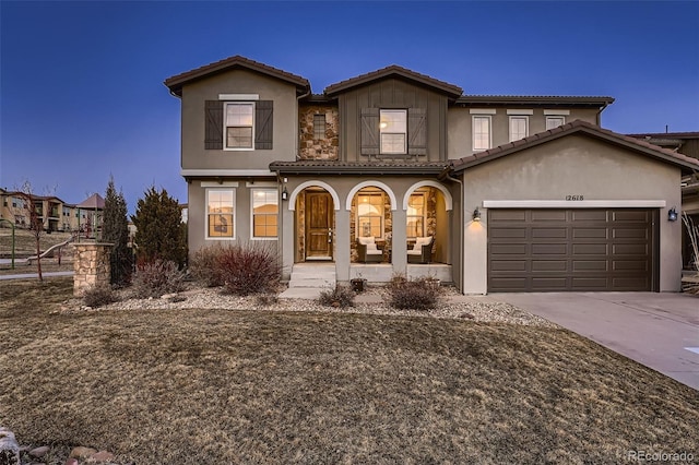 view of front of house with driveway, a tile roof, an attached garage, covered porch, and stucco siding