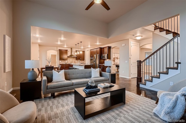 living area featuring baseboards, arched walkways, ceiling fan, stairway, and wood finished floors