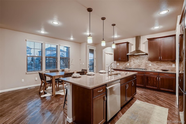 kitchen with dark wood-style floors, stainless steel appliances, tasteful backsplash, a sink, and wall chimney range hood