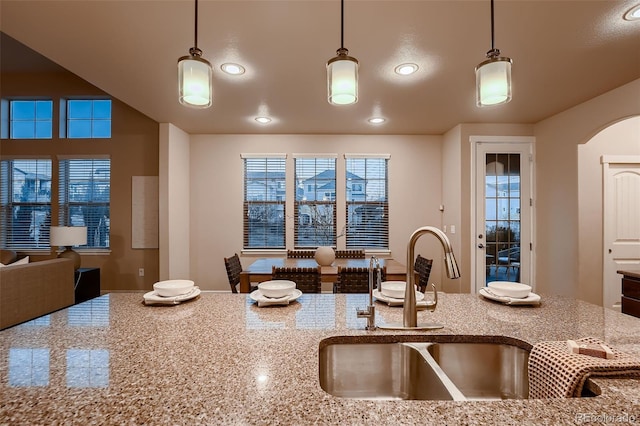 kitchen with arched walkways, light stone counters, hanging light fixtures, a sink, and recessed lighting