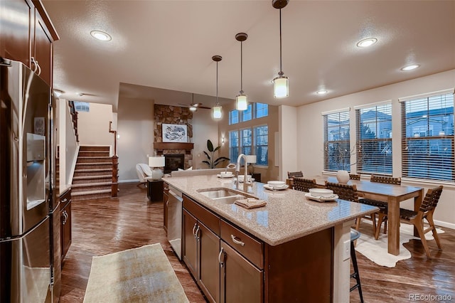 kitchen with a stone fireplace, a breakfast bar area, stainless steel appliances, dark wood-style flooring, and a sink