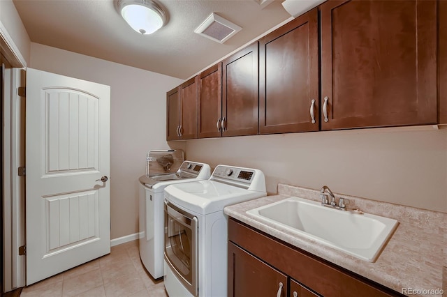 washroom with cabinet space, light tile patterned floors, visible vents, washing machine and clothes dryer, and a sink