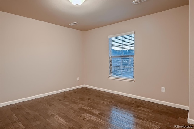 empty room with dark wood finished floors, visible vents, and baseboards