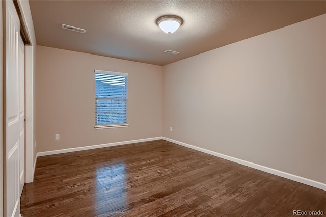 empty room with baseboards, a textured ceiling, visible vents, and dark wood-style flooring