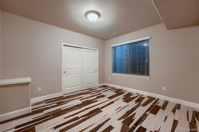 unfurnished bedroom with baseboards, visible vents, a closet, and wood finished floors