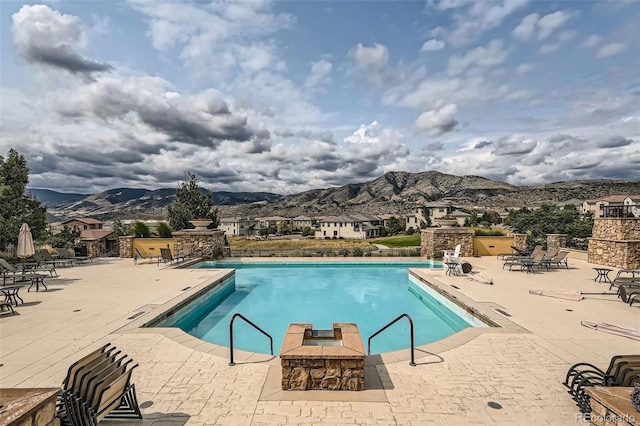 community pool with an outdoor fireplace, a mountain view, and a patio