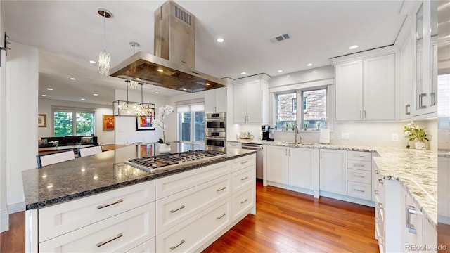 kitchen with light wood-style floors, white cabinets, visible vents, island exhaust hood, and stainless steel appliances