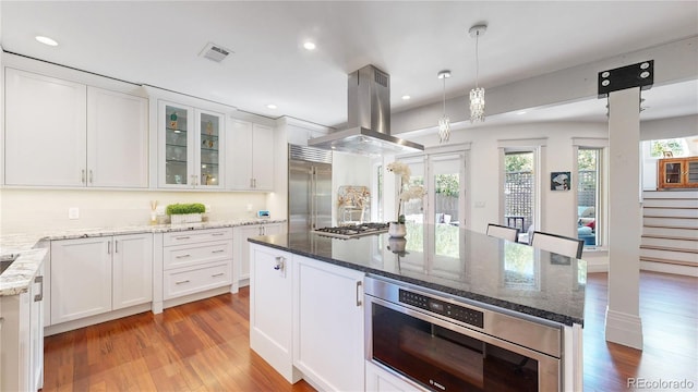 kitchen with visible vents, white cabinets, appliances with stainless steel finishes, light wood-style floors, and island range hood