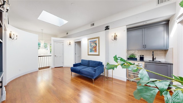 sitting room featuring a skylight, baseboards, light wood-style flooring, visible vents, and wine cooler