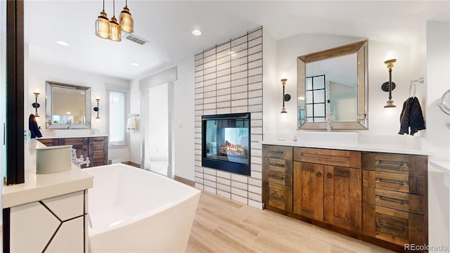 bathroom featuring two vanities, a multi sided fireplace, visible vents, wood finished floors, and a freestanding bath