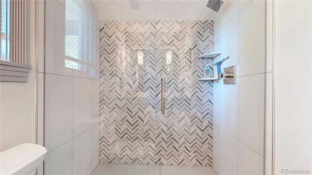 bathroom featuring a tile shower, a decorative wall, and toilet
