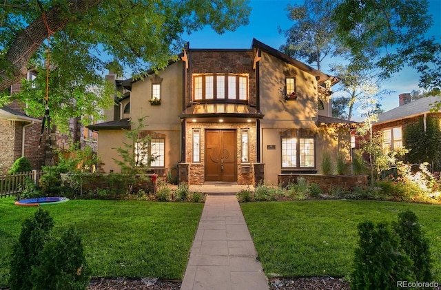 view of front of property featuring a front yard, stucco siding, stone siding, and fence