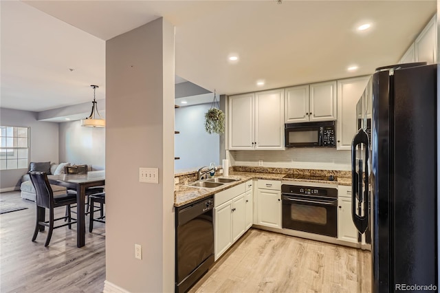 kitchen featuring light stone counters, light wood finished floors, white cabinetry, a sink, and black appliances