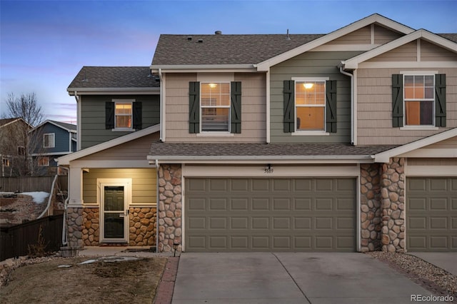 view of front of property with stone siding, fence, roof with shingles, concrete driveway, and an attached garage