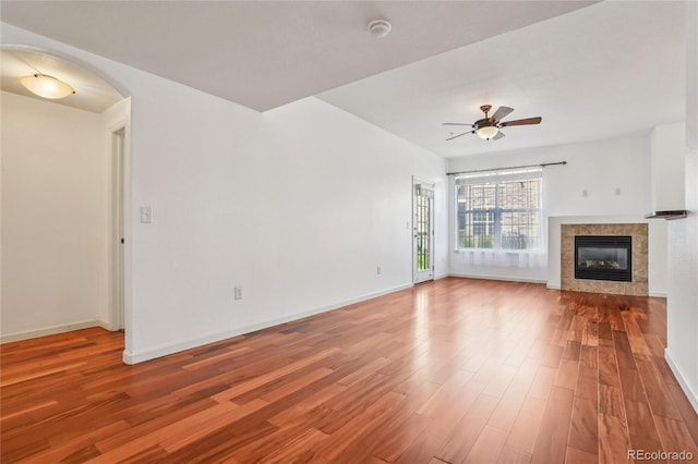 17442 Nature Walk Trl Unit 107, Parker, CO 80134 - unfurnished living room featuring arched walkways, wood finished floors, a tiled fireplace, and a ceiling fan