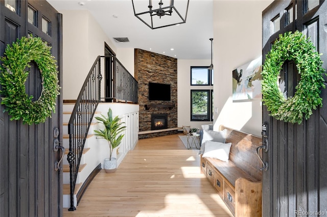 interior space with stairway, a stone fireplace, light wood-type flooring, a notable chandelier, and visible vents