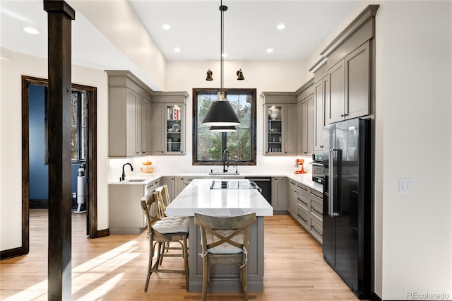kitchen with a center island, decorative backsplash, light wood-style floors, high end black fridge, and gray cabinetry